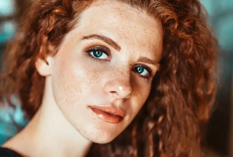 Primo piano di una ragazza con lentiggini e capelli rossi, con un trucco naturale che esalta la sua bellezza.